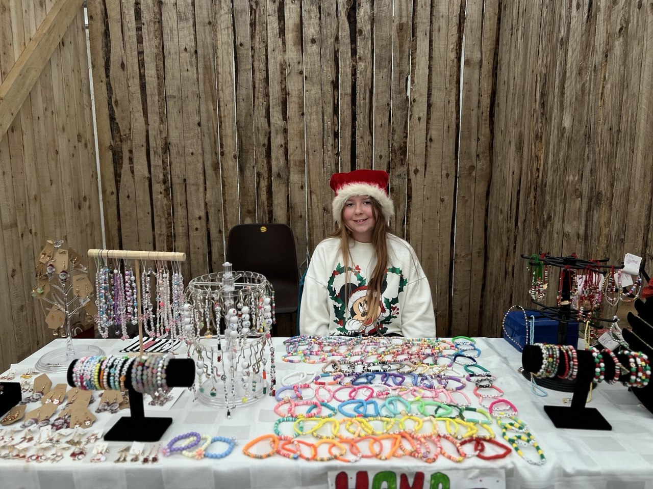 A girl in a Santa hat behind a table of colourful bracelets