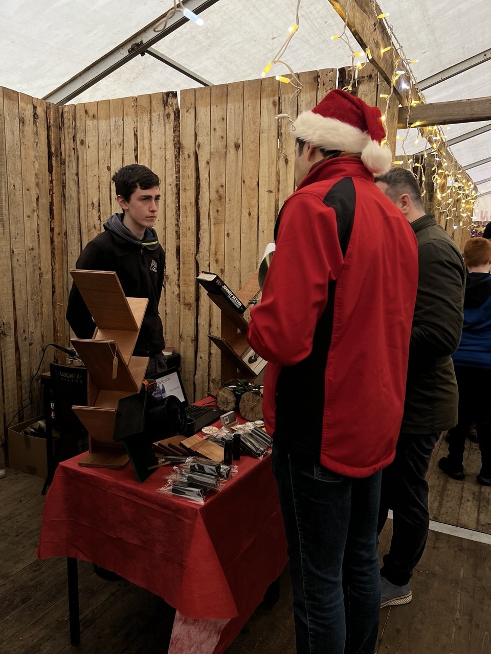 A judge in a Santa hat visits a young entrepreneur's wooden storage stall