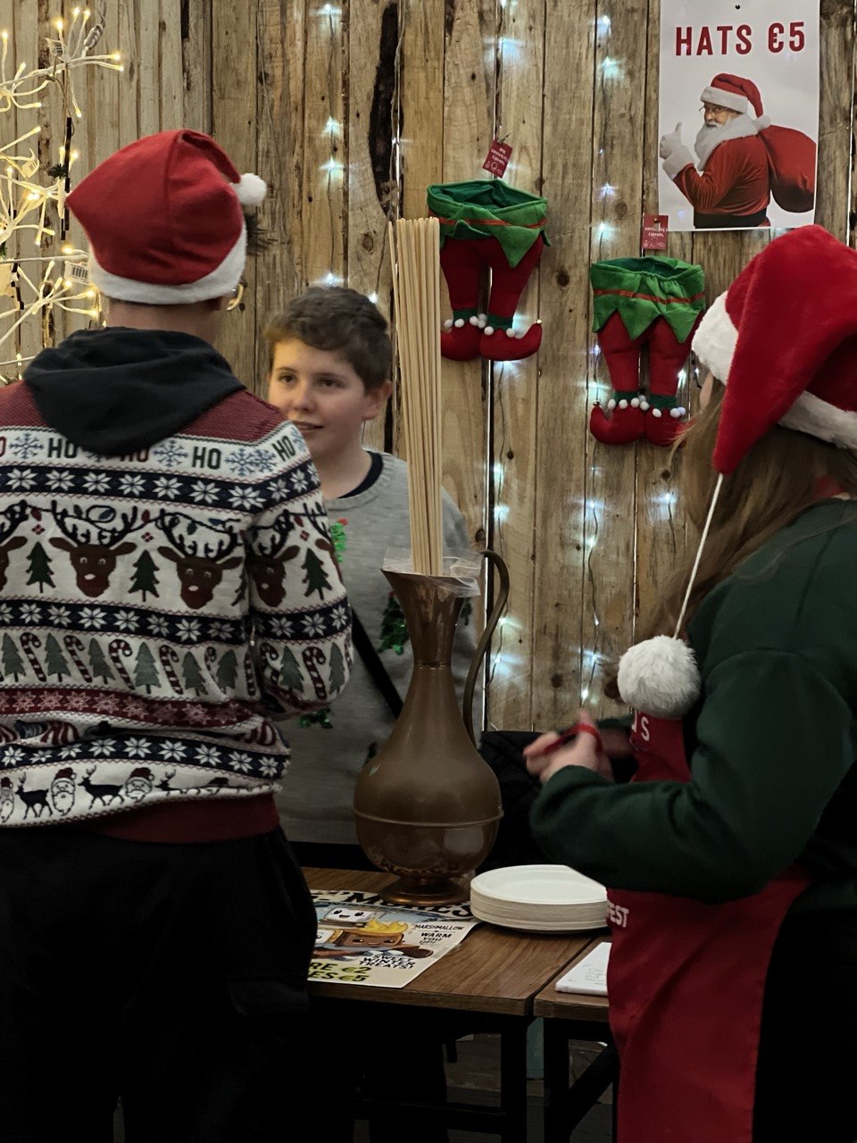 A boy serving customers in Santa hats at his stall